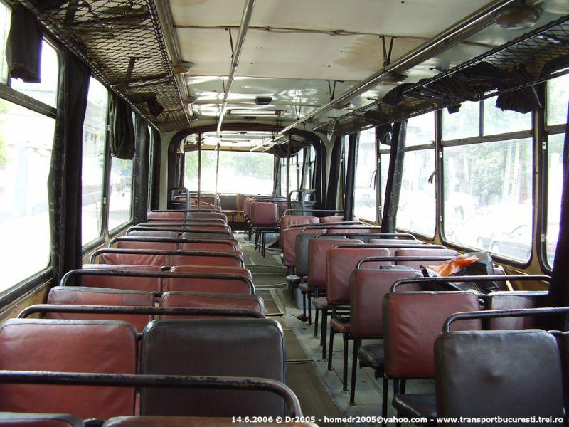Interiorul unui autobuz vechi din București, cu scaune roșii și portbagaje metalice.